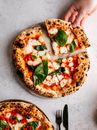 A top view of a fresh Margarita pizza with a hand taking a slice, featuring basil and mozzarella.