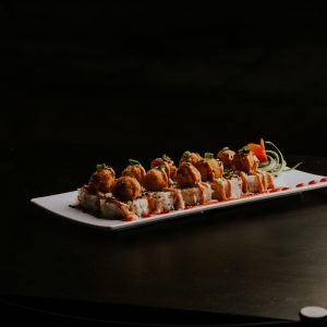 Gourmet sushi roll with crispy tempura topping, garnished with vegetables on a black background.