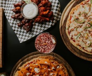 A mouthwatering spread of pizzas and chicken wings with a refreshing drink, perfect for sharing.